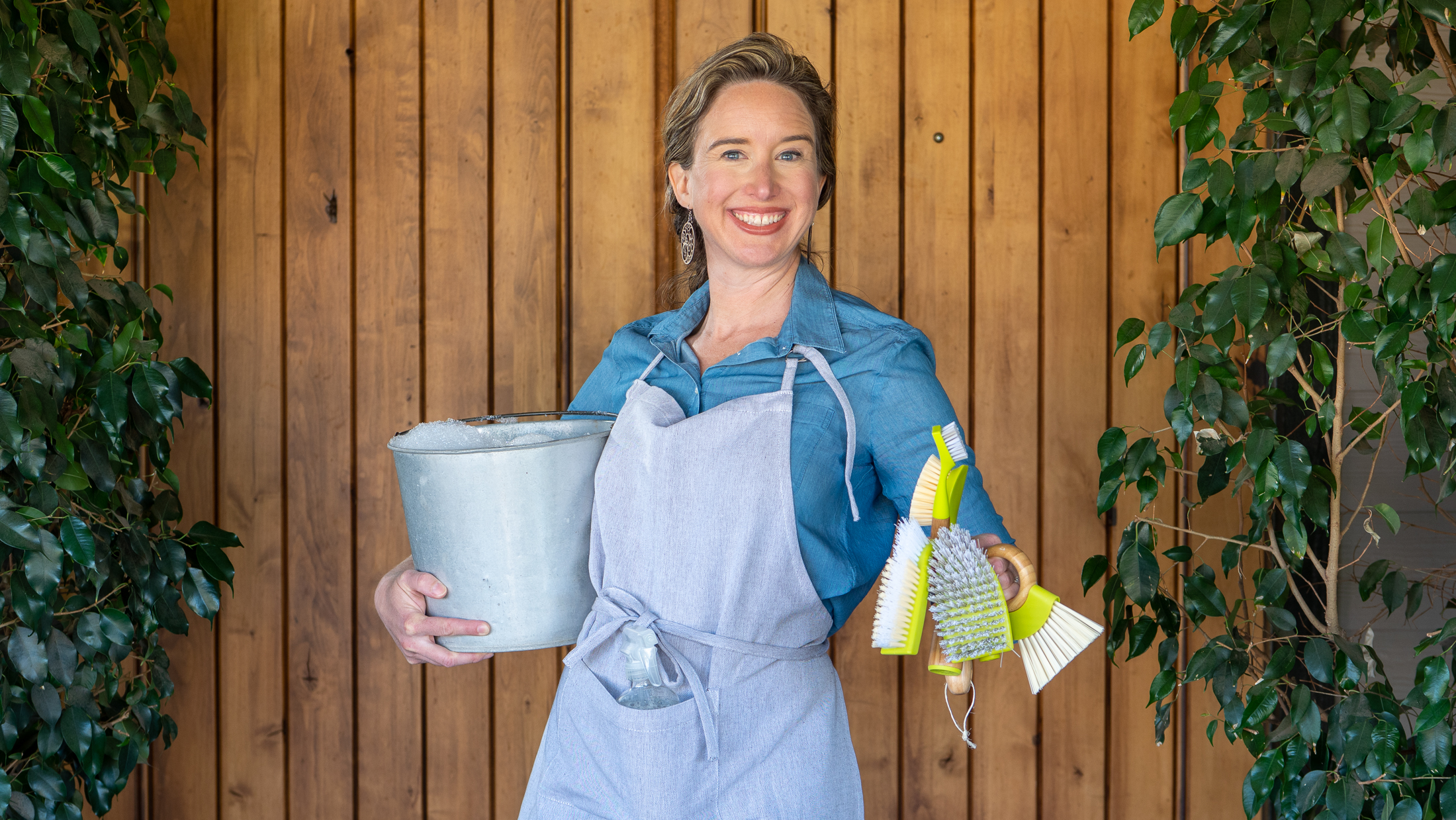 Lisa holding a metal pail in one hand and green cleaning tools in the other.