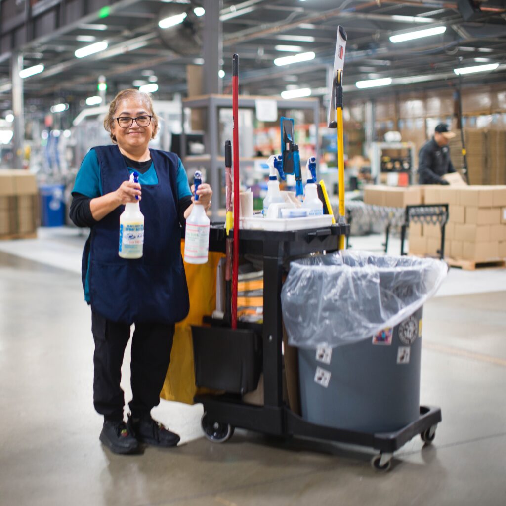 Azucena, a member of the Dr. Bronner's custodial team, smiling in front of her cleaning cart.