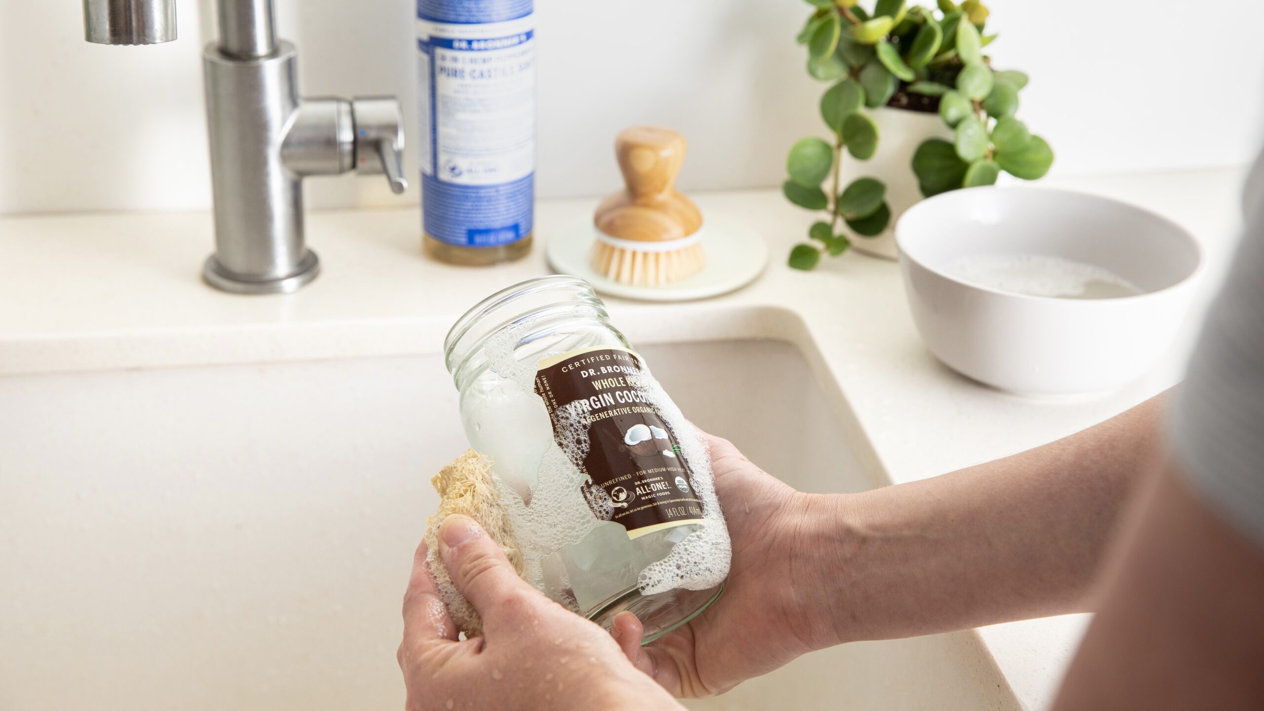 Person scrubbing label of Dr. Bronner's Virgin Coconut Oil jar.