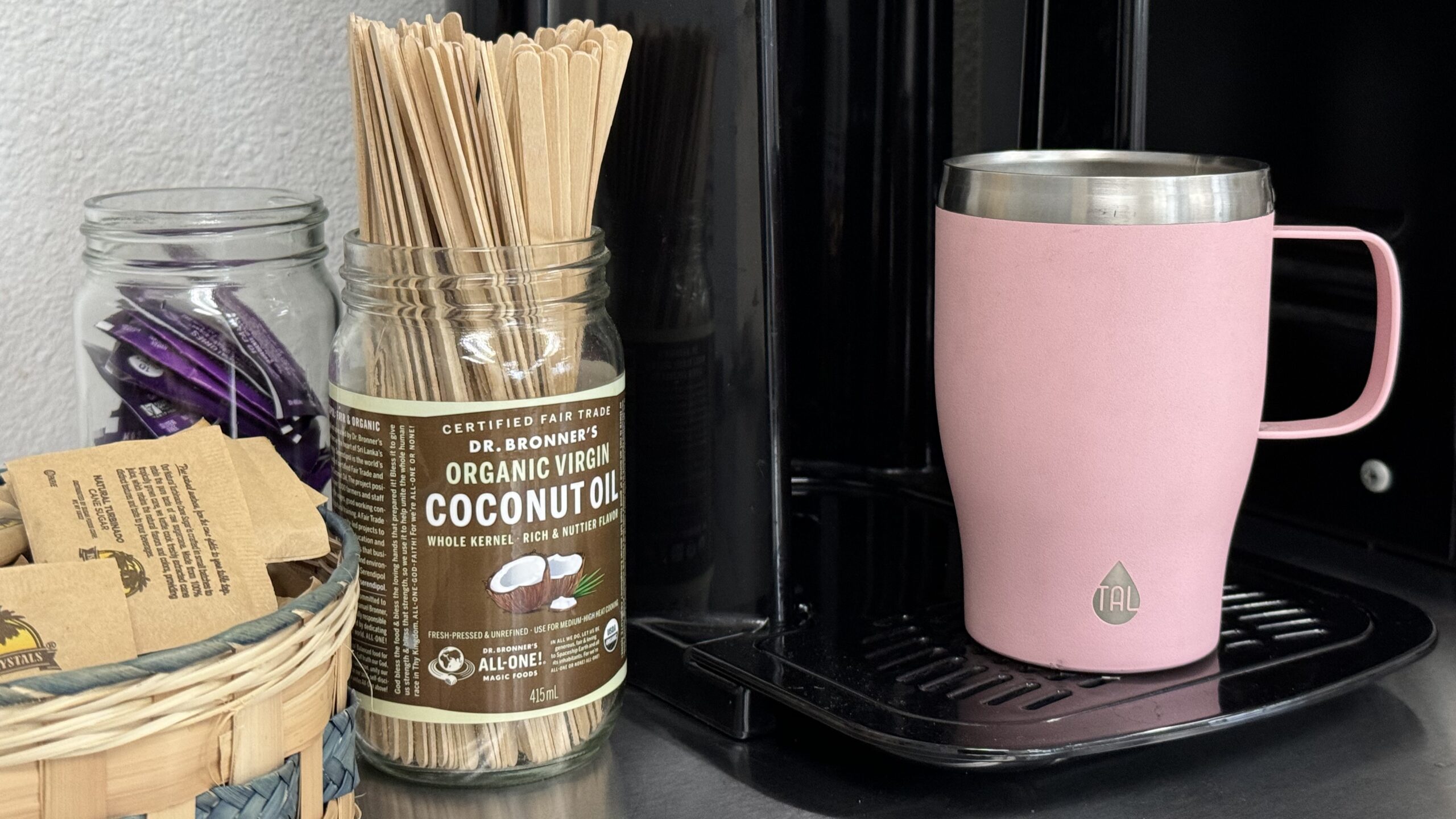 Coconut oil jar with coffee stir sticks next to a coffee maker.