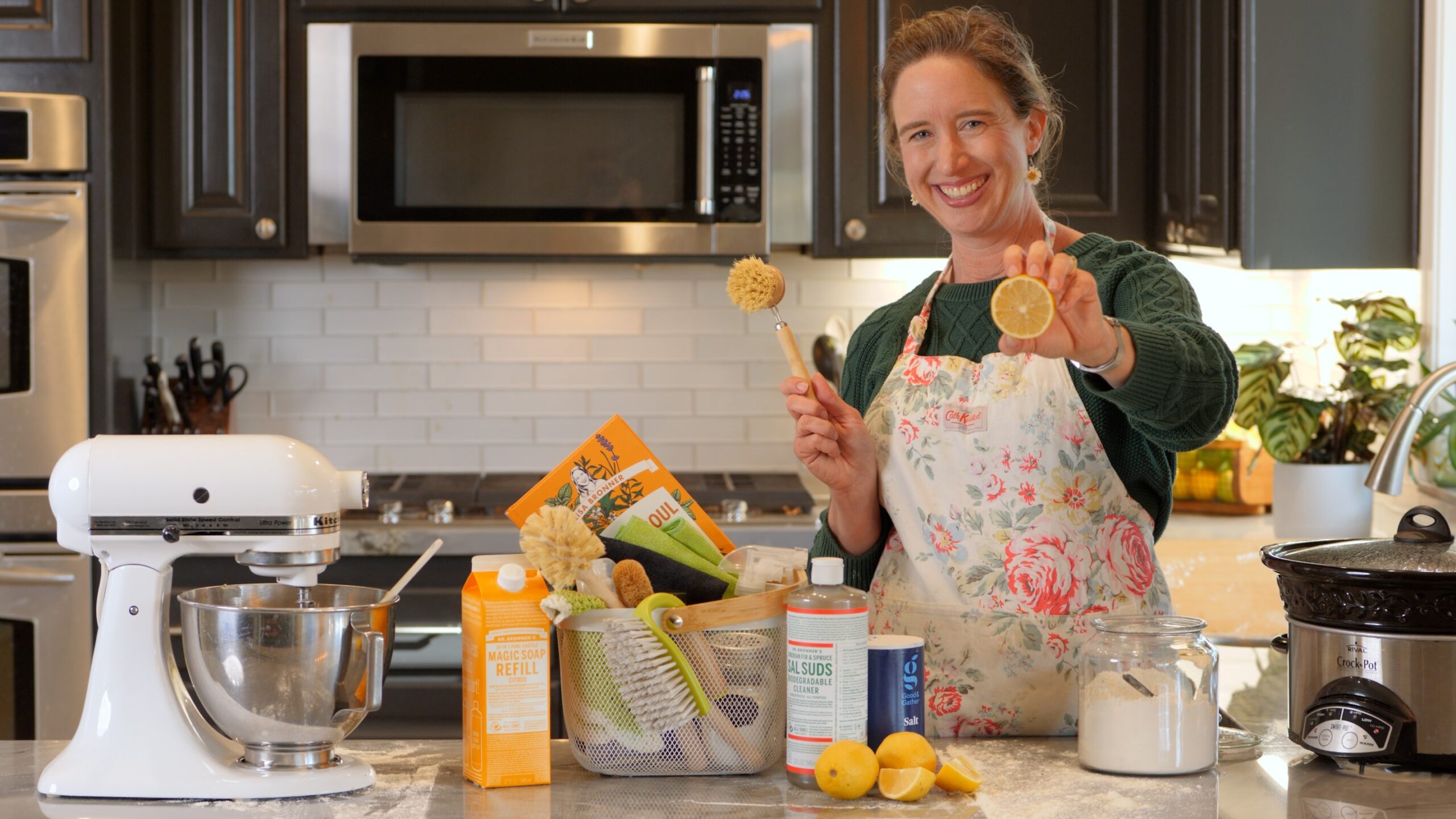 Lisa Bronner holding up a lemon, smiling, in her kitchen with cleaning supplies.